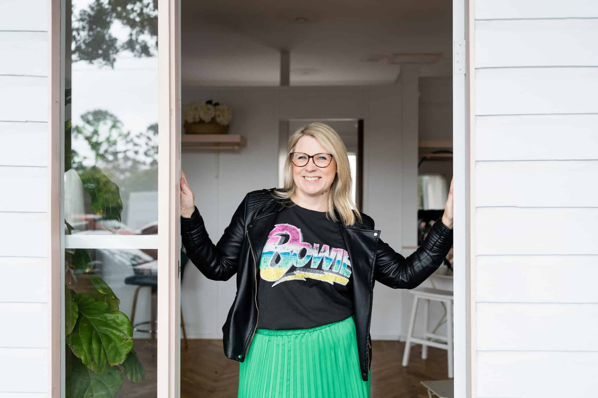 A WordPress designer wearing glasses and a green skirt standing in front of a white house.