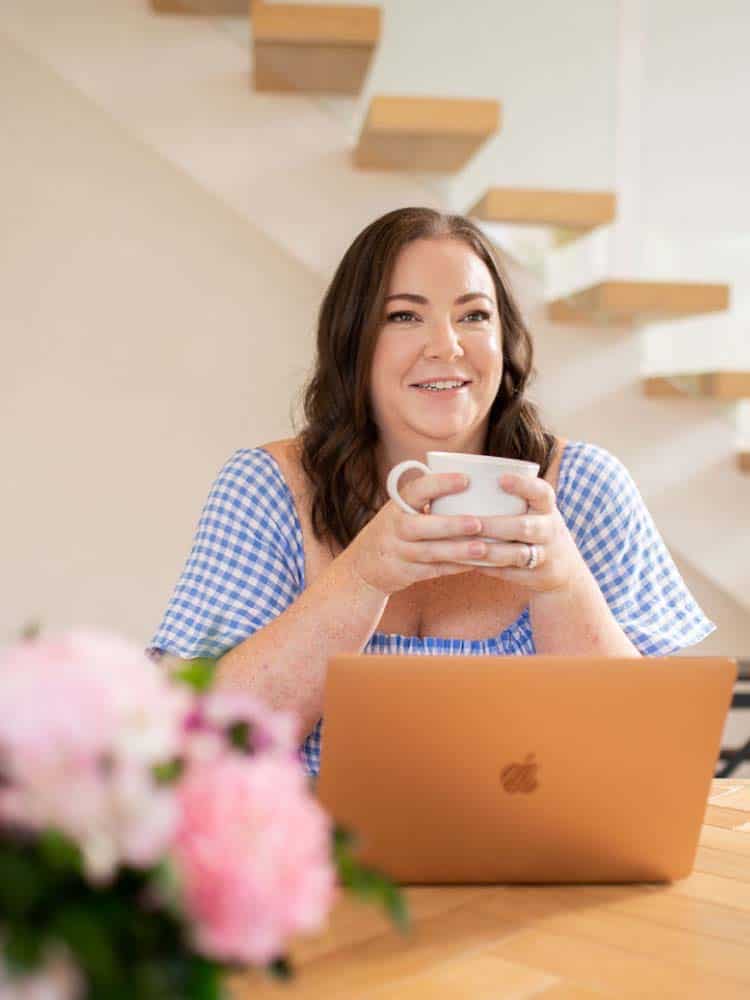 A woman sitting at a table with a laptop and a cup of coffee.