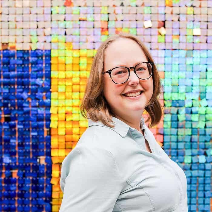 Woman smiling in front of a colorful tiled wall.